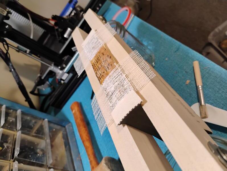 A photo of the clamp in action from a jaunty angle to better show the fresh glue and mull being applied to the old spine.