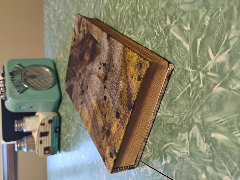 A photo of the completed book used to show the found painted canvas I used for the book's cover. It's a moody splash of greys, black and yellow that has a certain weathered quality to it.