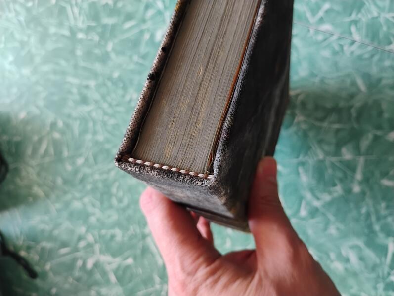 A photo showing the top edge of the completed book to illustrate where the head banding goes and how it looks when finished. The head banding used here is a checkered brown and white design, extremely common for case-bound books.