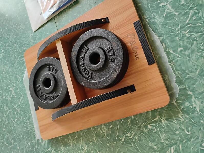 A photo showing four 5 pound iron weigts pressing down an upside-down balance board to make a janky-ass press, necessary for ensuring the cloth cover remains firm and flat against the cardboard as the glue dries.