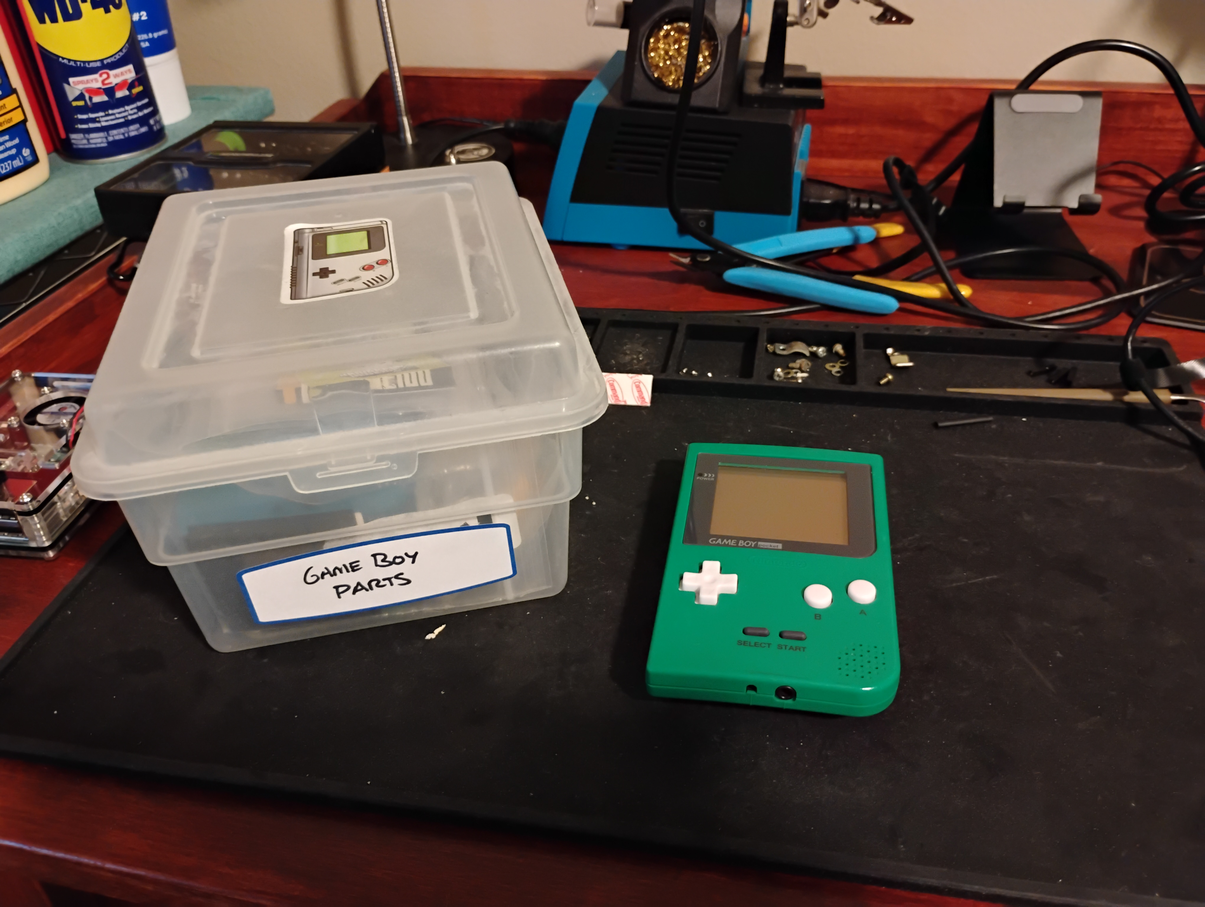 photo of my workbench featuring a small box of leftover Game Boy parts and my old green Game Boy Pocket